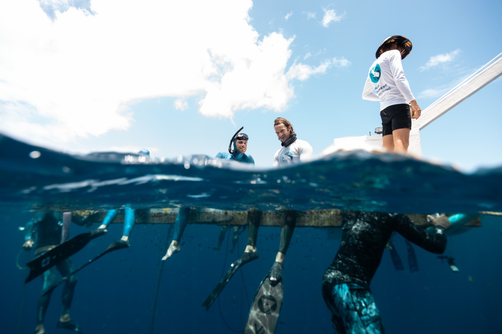 Over-under view at the Blue Element platform — freedivers at the surface and finning below, Soufrière Bay, Dominica