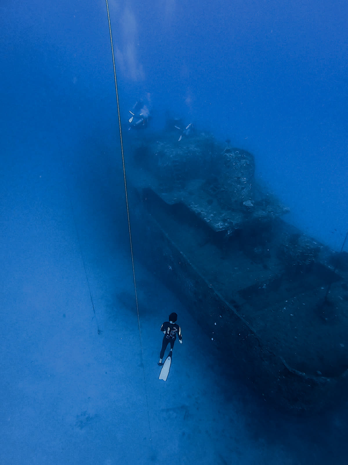 Harry McCahill freediving down toward a shipwreck in the deep blue off Hawai'i